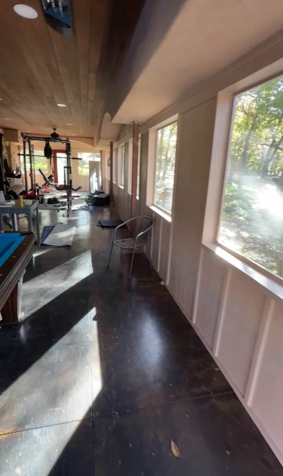Enclosed patio in use as a gym and game room, with a stained concrete floor and a row of windows, built by MASB Construction