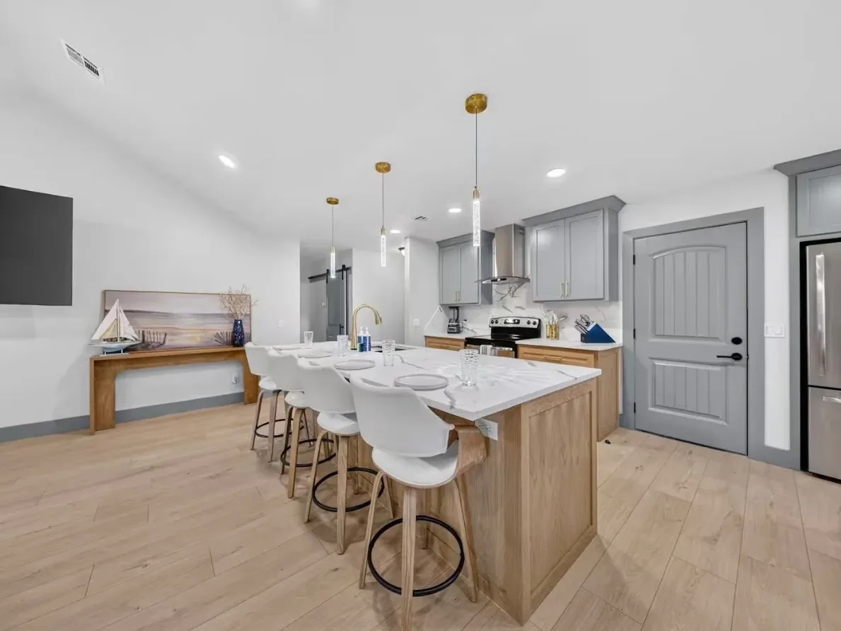 White-oak kitchen island seating four under gold pendant lights, with gray upper cabinets, in a Piedmont kitchen remodeled by MASB Construction