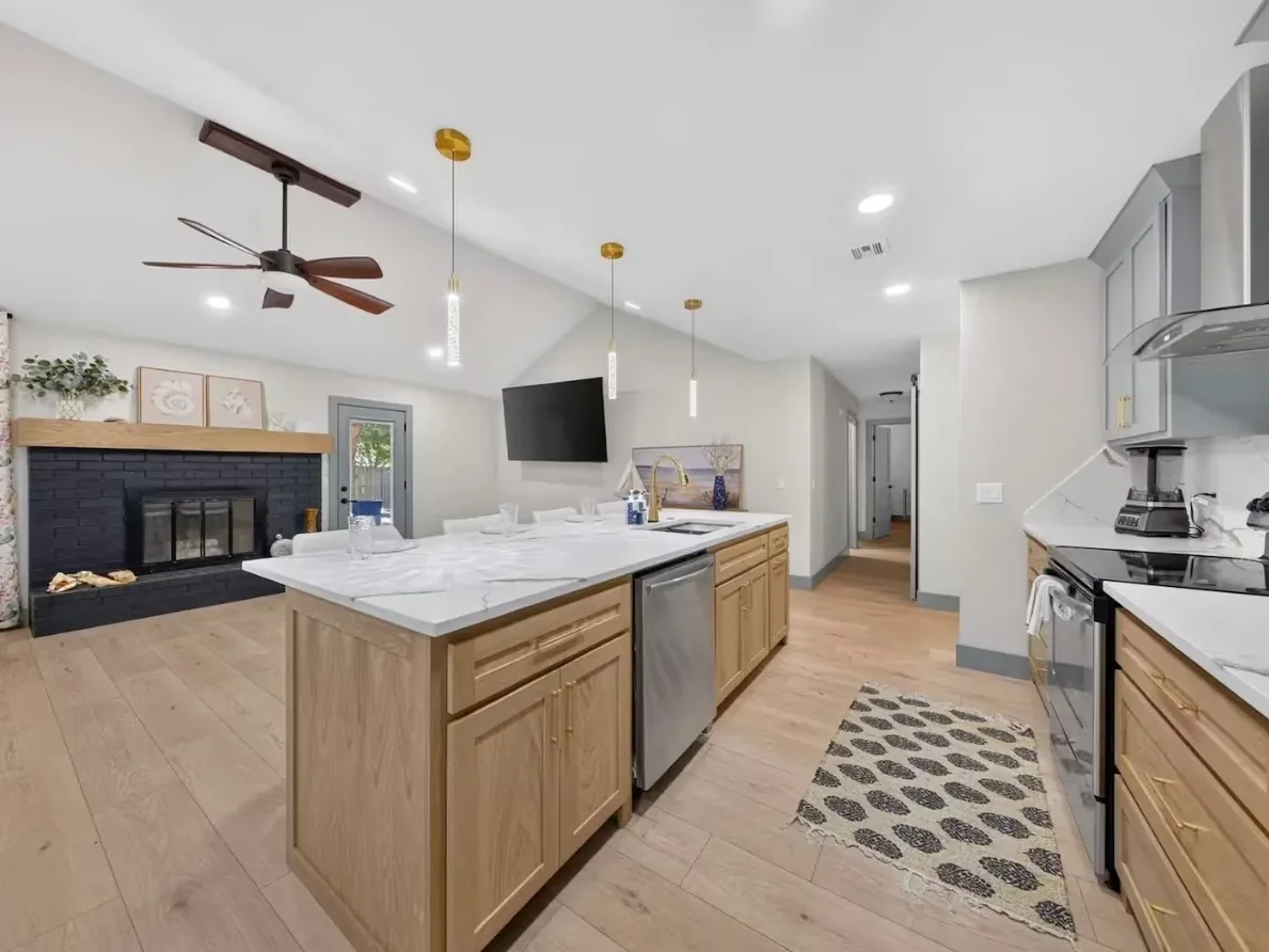 Quartz-topped white-oak island looking toward the painted brick fireplace under a vaulted ceiling in a Piedmont kitchen remodeled by MASB Construction