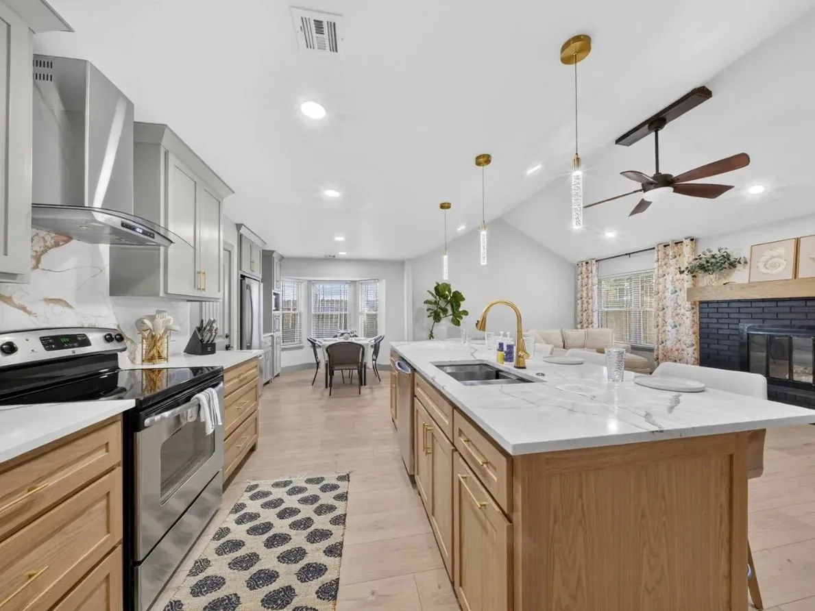 Opened-up kitchen in a Piedmont whole-home remodel by MASB Construction: white-oak island, quartz backsplash, bay-window dining nook, and brick fireplace beyond
