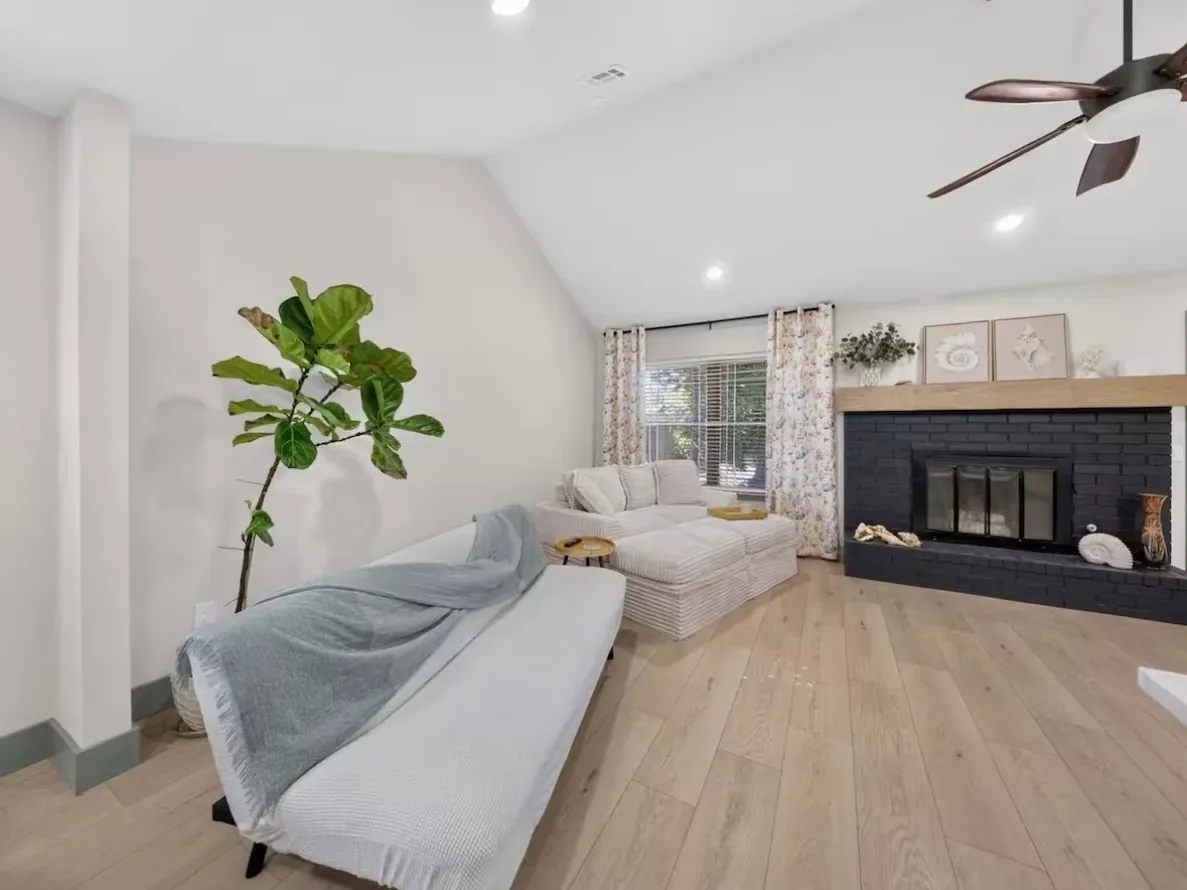 Living room under a vaulted ceiling with a painted brick fireplace and wood mantel in a Piedmont whole-home remodel by MASB Construction