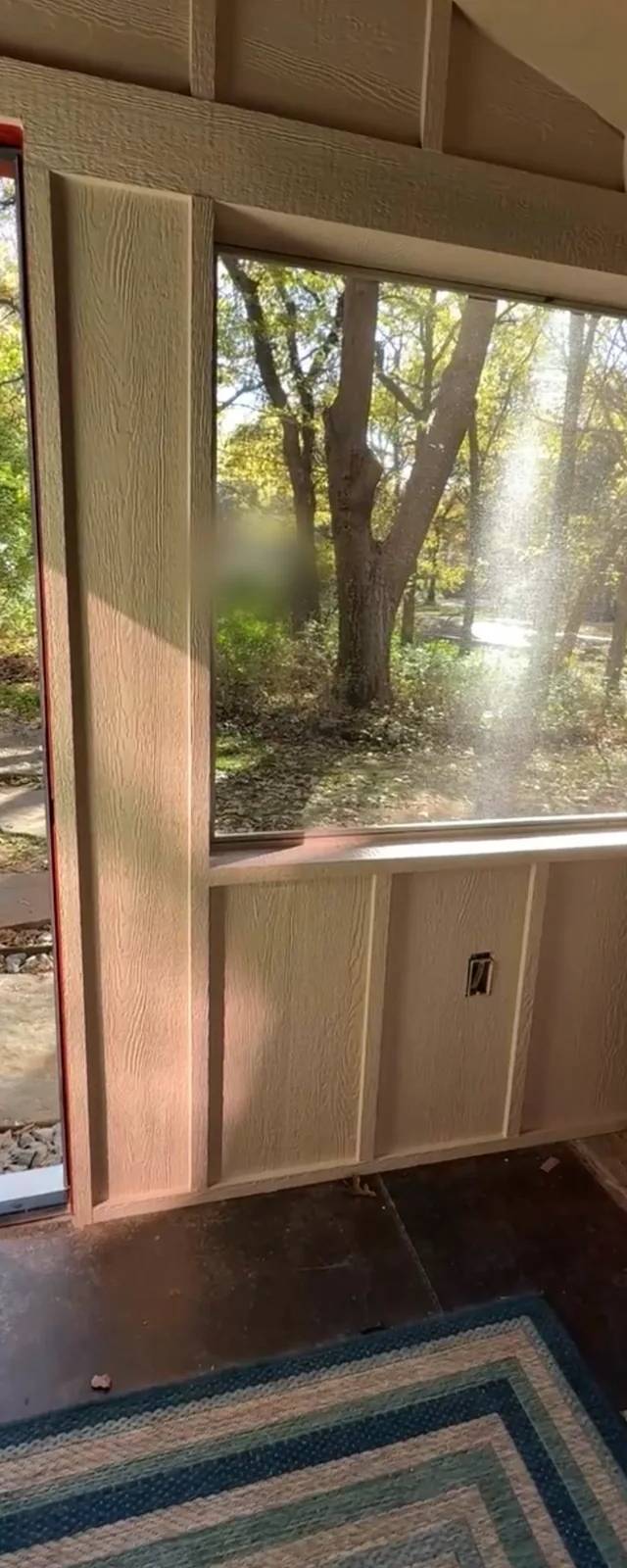 Inside the new room: a large window over board-and-batten paneling, a stained concrete floor, and an original porch post at the edge