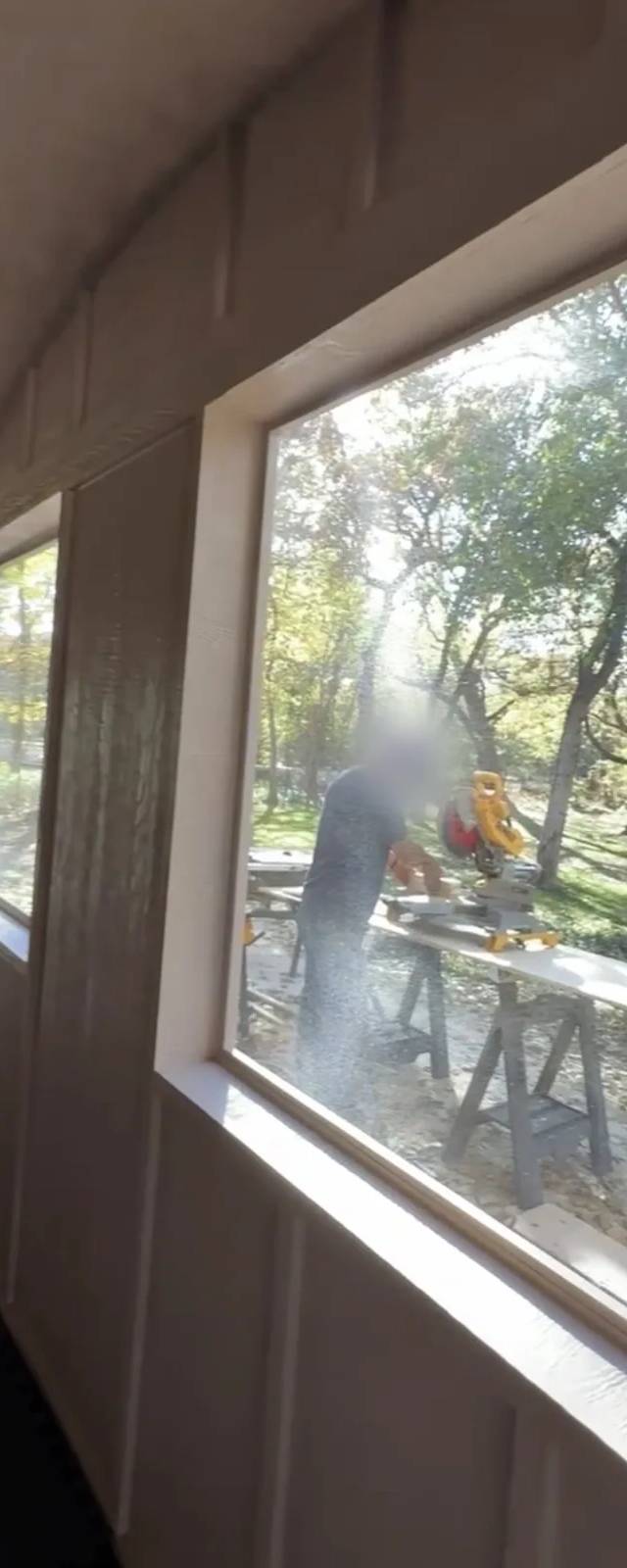During the build: a crew member cuts trim at a miter saw outside the new windows