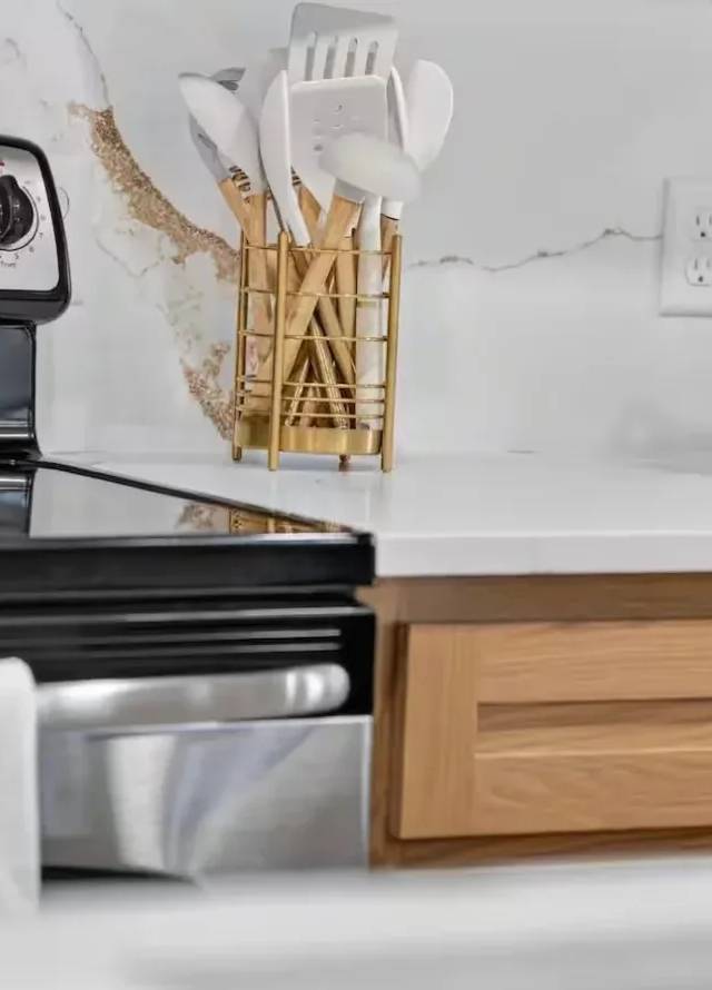 Electric range against a full-height white quartz backsplash with gold veining, beside a white-oak drawer with a gold pull