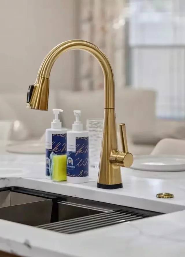 Gold pull-down faucet over a stainless workstation sink set in a white quartz island