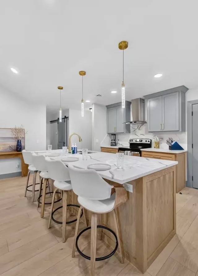 White-oak kitchen island seating four under gold pendant lights, with gray upper cabinets and a stainless refrigerator, in a Piedmont whole-home remodel