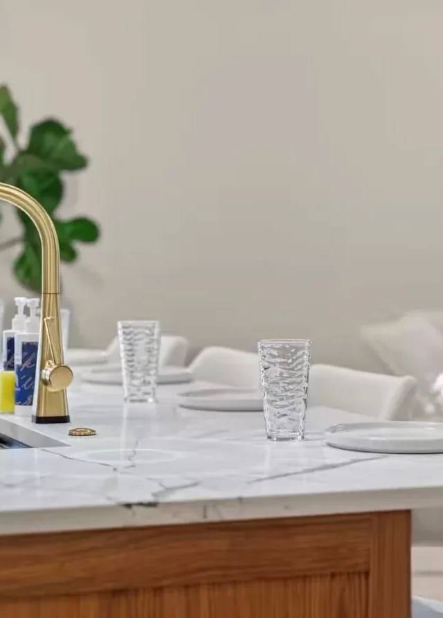 Gold faucet and white quartz island set with plates and glasses in a Piedmont kitchen