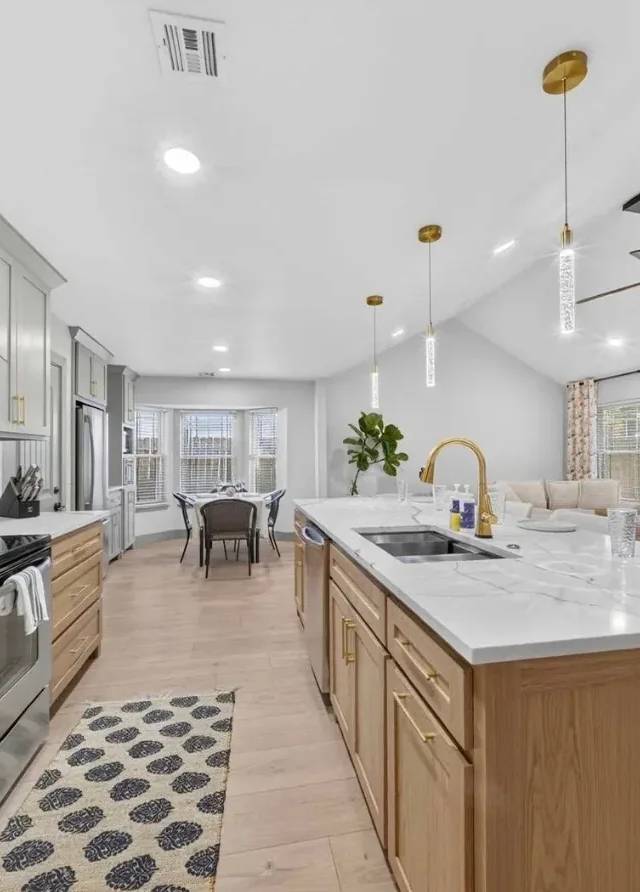 Opened-up kitchen in a Piedmont whole-home remodel: range wall with quartz backsplash, white-oak island with gold faucet, bay-window dining nook, and brick fireplace beyond