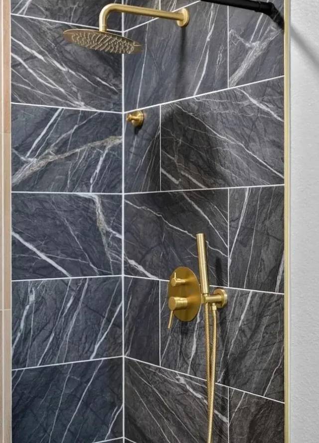 Dark marble shower walls with a gold rain head and handheld shower beside a wood-slat accent wall