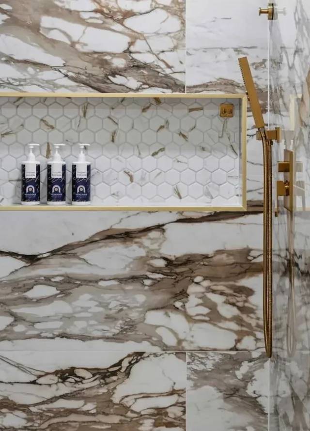 Shower niche in white hexagon mosaic framed with gold trim, set in white-and-gold marble