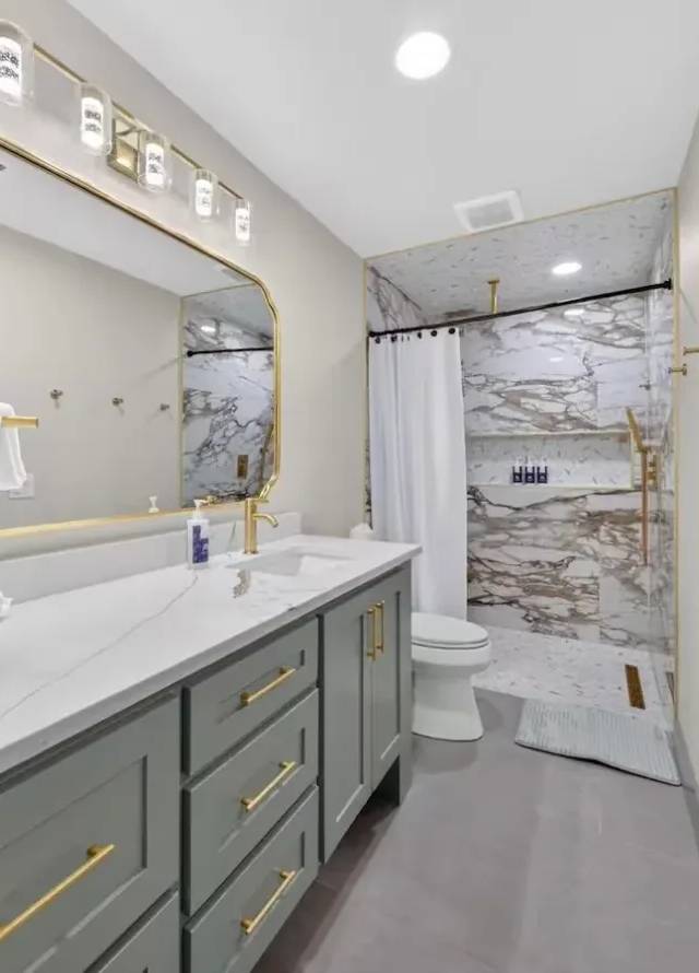 Second bathroom: long gray vanity with a quartz top, gold-framed mirror, and walk-in shower in white-and-gold marble