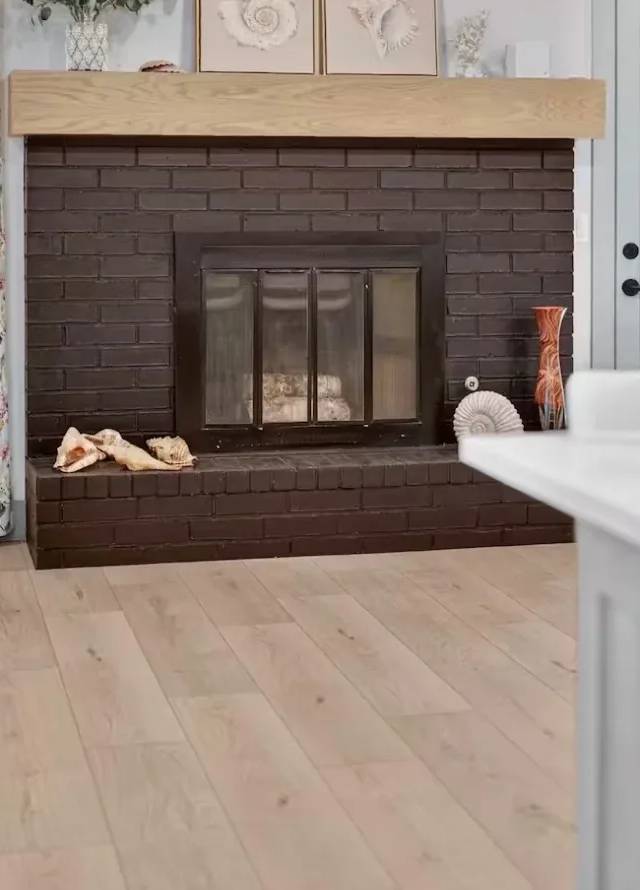 Dark painted brick fireplace with a wood mantel beside light wood-look flooring in a Piedmont living room