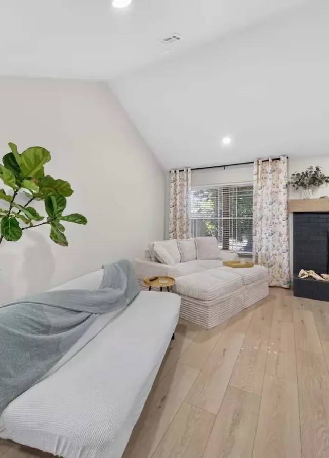 Living room under a vaulted ceiling with a dark painted brick fireplace and wood mantel in a Piedmont whole-home remodel